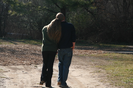 A couple walking closely together on a nature trail.